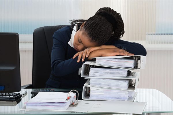 tired business woman sleeping at work on top of her binders of documents