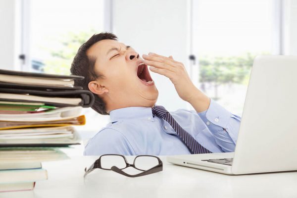Office worker yawning from exhaustion with documents piled on his desk