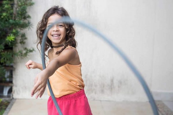 young girl with a hula hoop on her arms smiling
