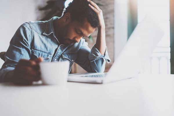 Man sitting at desk with head down and coffee in hand looking exhausted