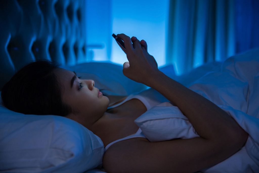 woman awake looking at her phone in bed